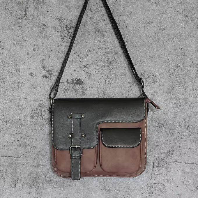Borsa a tracolla in pelle nera e marrone con fibbia e tasche frontali, design elegante su sfondo grigio. Accessorio moda donna.