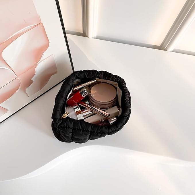 Borsa cosmetica nera su tavolo bianco con trucchi, rossetti e cipria. Design elegante, accessori bellezza, organizzazione trucco.