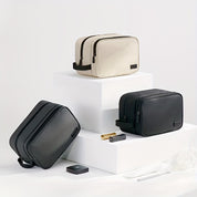 Tre eleganti beauty case in pelle nera e beige su piedistalli bianchi, ideali per viaggi. Design moderno, alta qualità, accessori da bagno inclusi.