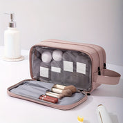 Borsa da toilette rosa con scomparti trasparenti, contenente pennelli trucco e flaconi. Organizer cosmetici da viaggio, elegante e funzionale.