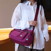 Donna con camicia bianca indossa borsa a tracolla viola con zip e tasche multiple. Accessorio moda elegante, perfetto per uso quotidiano.