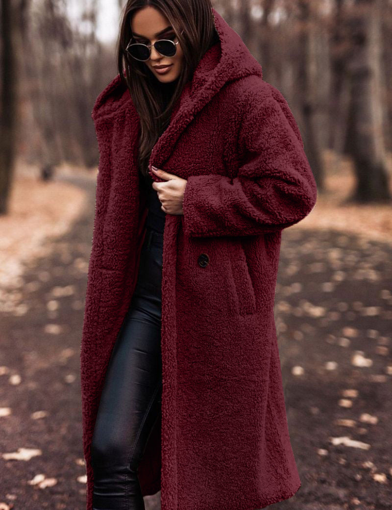 Donna con cappotto teddy borg rosso, occhiali da sole, pantaloni neri in pelle, in un parco autunnale. Moda invernale, stile casual chic.