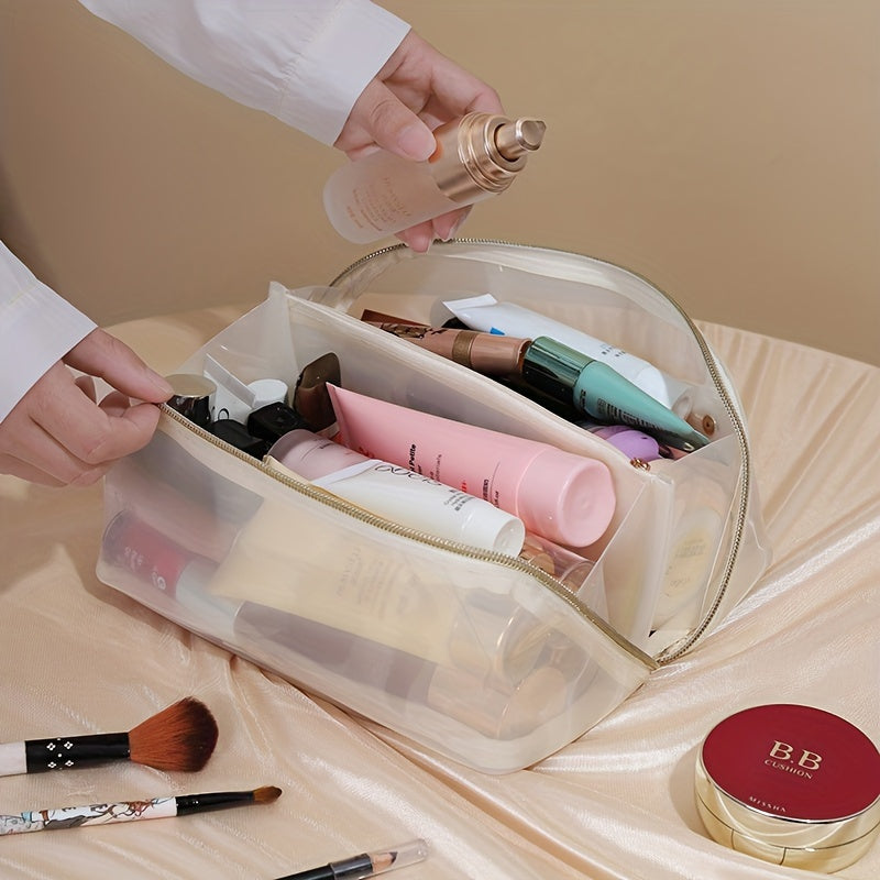 Borsa trasparente per cosmetici con cerniera, contenente creme, trucchi e pennelli su sfondo beige. Ideale per organizzare prodotti di bellezza.
