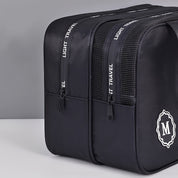 Zaino da viaggio nero con doppia cerniera, logo "M" e scritta "Light Travel". Design moderno, ideale per viaggi e uso quotidiano.