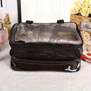 Borsa trasparente in PVC nero per cosmetici, con cerniera e manici, su tavolo con fiori e prodotti di bellezza. Ideale per organizzare trucchi.