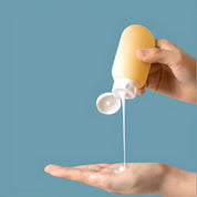 Mani versano lozione bianca da flacone giallo su sfondo blu. Cura della pelle, idratazione, cosmetici. Flacone cosmetico, prodotto per la pelle.