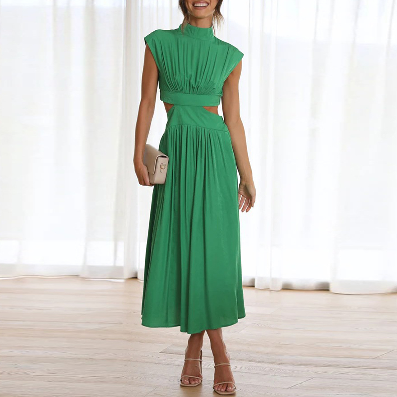 Abito lungo verde elegante con cut-out laterali, senza maniche, indossato da una donna con sandali e pochette beige, sfondo con tende bianche.