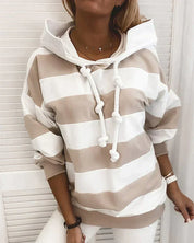 Felpa a righe bianche e beige con cappuccio e lacci spessi, indossata da una donna. Moda casual, abbigliamento autunnale, stile confortevole.
