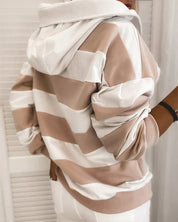 Felpa a righe bianche e beige, con cappuccio, indossata da una persona di spalle. Moda casual, abbigliamento autunnale, stile urbano.