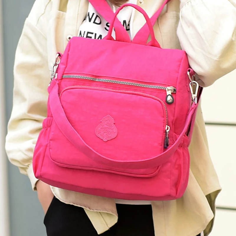 Zaino rosa vivace con tasche multiple e cerniere, indossato da una persona. Design moderno, ideale per scuola o viaggio. Accessorio moda trendy.