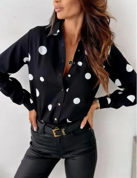 Camicia nera a pois bianchi, donna in posa elegante, pantaloni in pelle nera, cintura con fibbia dorata, moda femminile, abbigliamento casual chic.