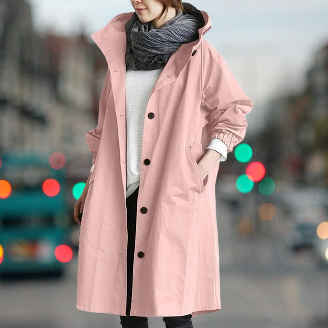 Donna con cappotto rosa lungo, sciarpa grigia e sfondo urbano sfocato. Moda autunnale, abbigliamento casual elegante, tendenze street style.
