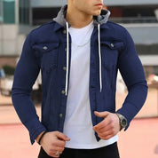 Giacca di jeans blu scuro da uomo con cappuccio grigio, indossata sopra una maglietta bianca. Stile casual, moda maschile, abbigliamento urbano.
