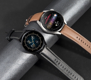Due smartwatch eleganti con cinturini in pelle marrone e nero, display digitale a colori, su sfondo grigio. Tecnologia indossabile moderna.