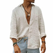 Camicia uomo in lino bianco, maniche lunghe, abbinata a pantaloni a righe blu. Stile casual estivo, accessori con bracciali e collane.