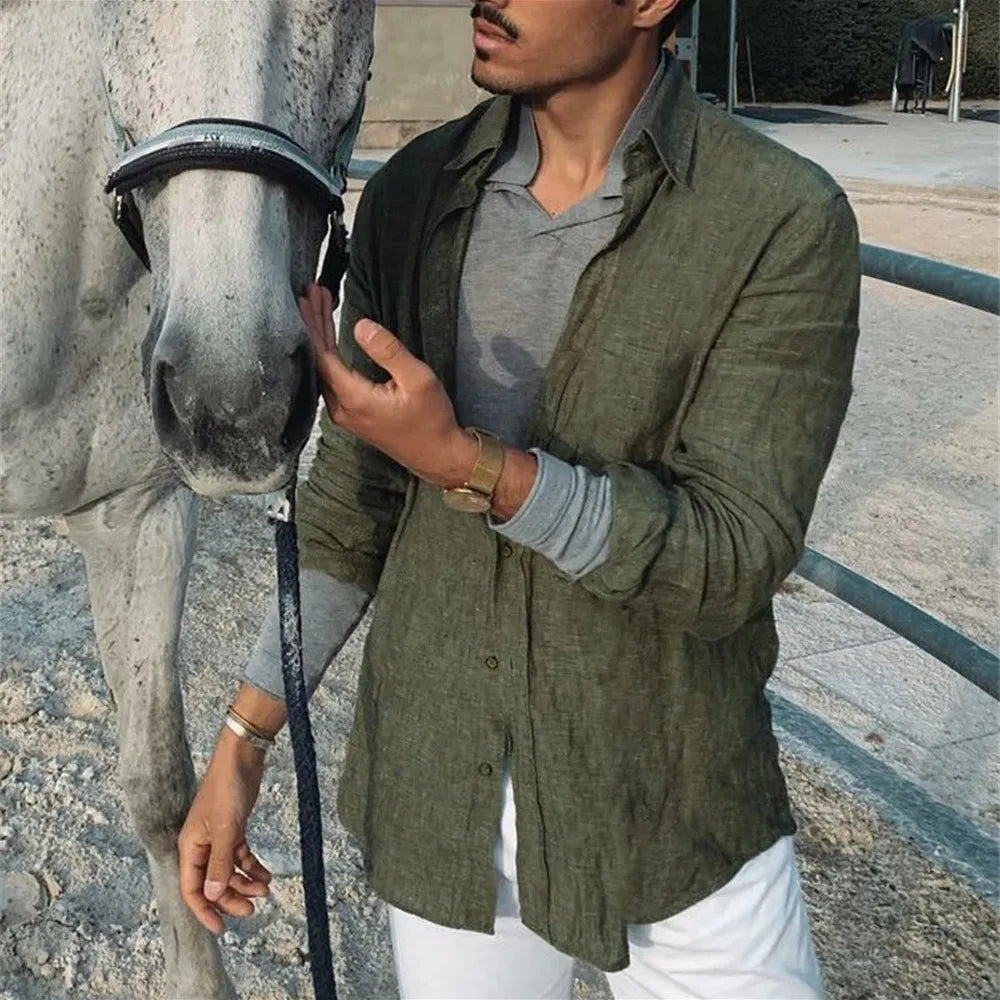 Uomo con camicia verde accanto a cavallo grigio in recinto. Moda casual maschile, equitazione, camicia di lino, pantaloni bianchi.