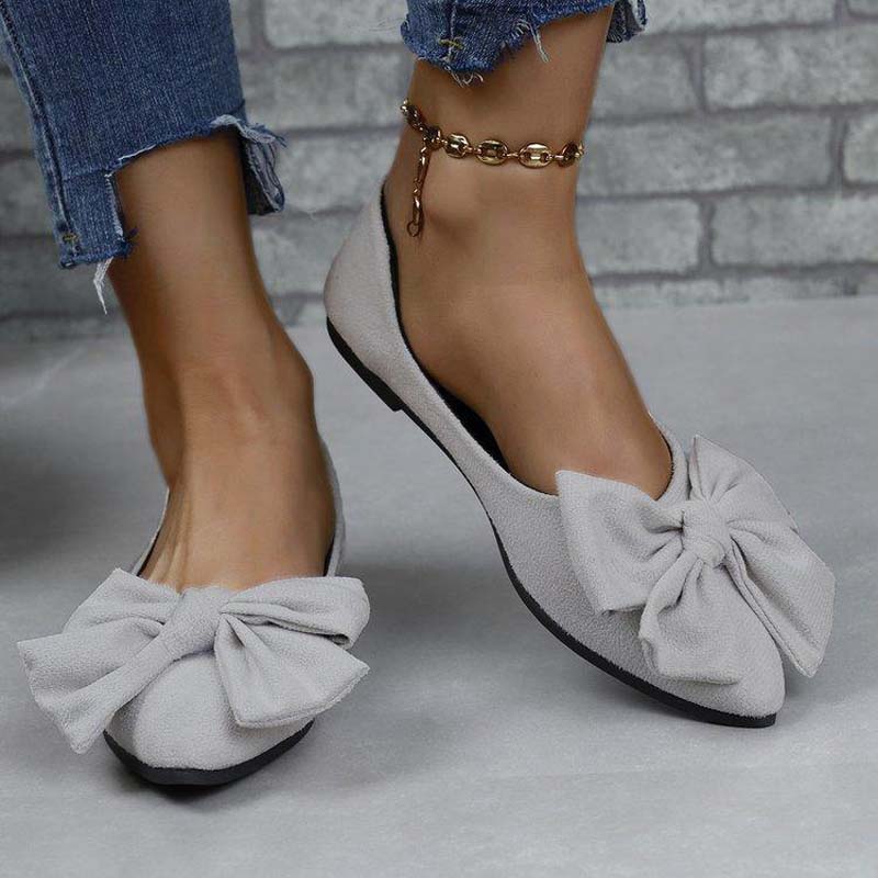 Scarpe ballerine grigie con fiocco grande, indossate su pavimento grigio. Design elegante, perfette per moda casual e abbigliamento quotidiano.