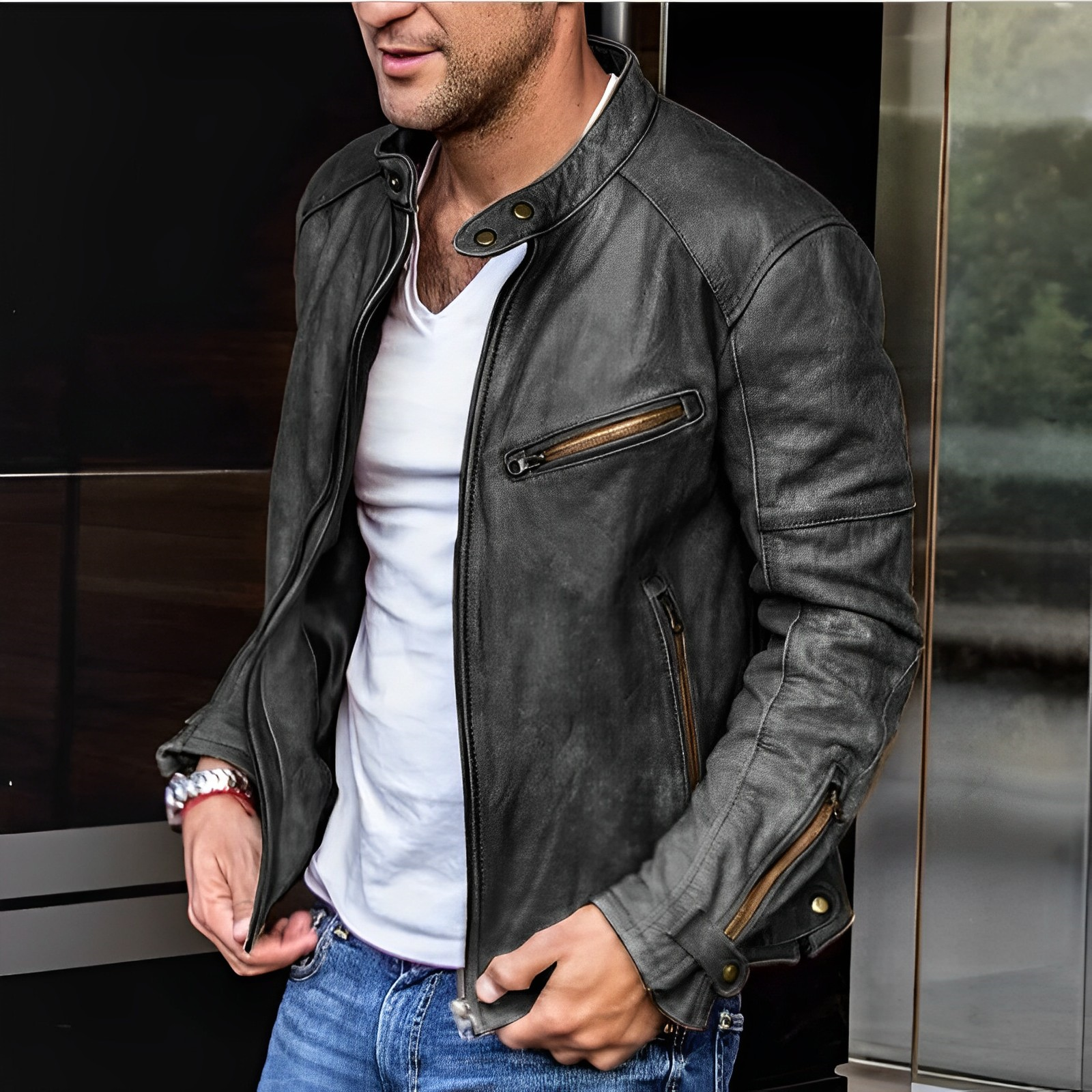 Giacca in pelle nera da uomo, stile motociclista, con zip e dettagli in metallo, indossata su maglietta bianca e jeans. Moda casual elegante.