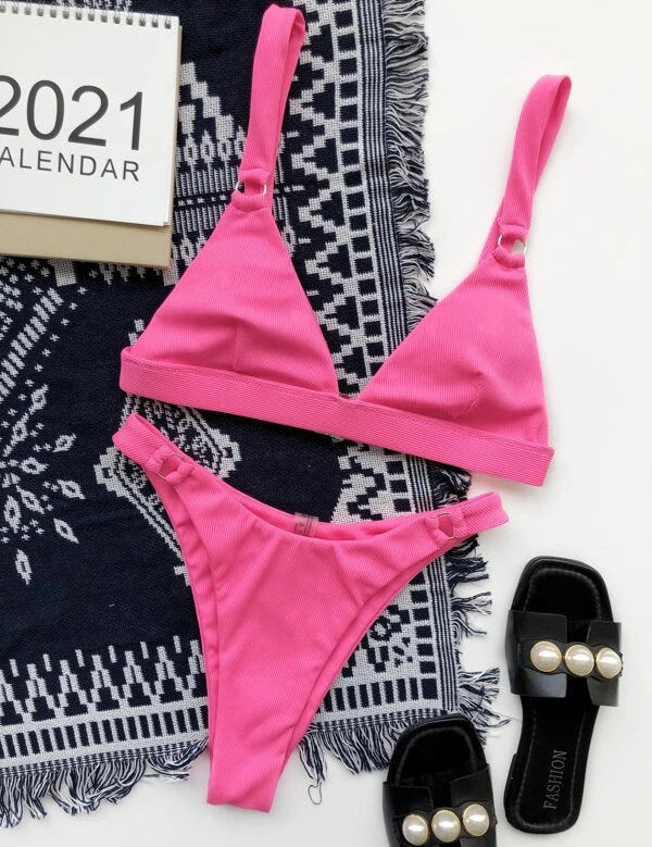 Bikini rosa a triangolo su tappeto blu con calendario 2021 e sandali neri con perle. Moda estiva, costumi da bagno donna, accessori mare.