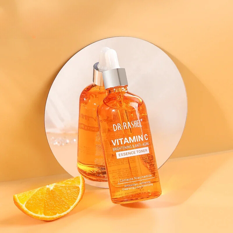 Bottiglia di tonico alla vitamina C Dr Rashel su sfondo arancione, riflessa in uno specchio. Include fetta d'arancia. Skincare illuminante e anti-età.
