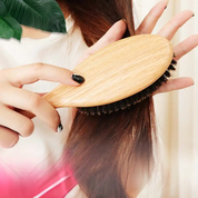 Donna che spazzola i capelli con spazzola in legno naturale, setole morbide. Cura capelli, accessori bellezza, spazzola eco-friendly.