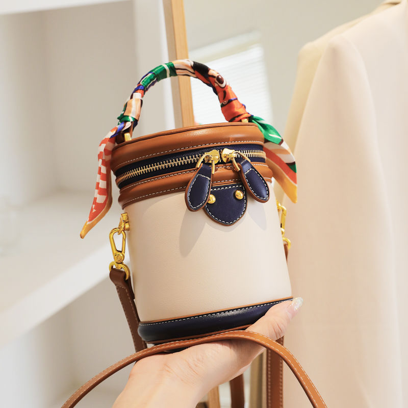 Borsa a secchiello in pelle bianca e marrone con dettagli blu, manico decorato con foulard colorato, design elegante e moderno, moda donna.