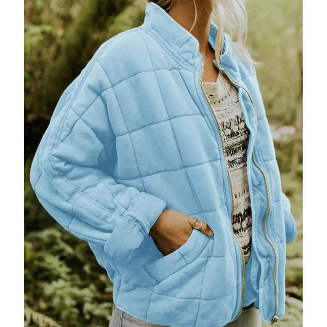 Giacca trapuntata azzurra da donna, con zip frontale e tasche laterali, indossata su maglia casual. Moda autunnale, abbigliamento outdoor.
