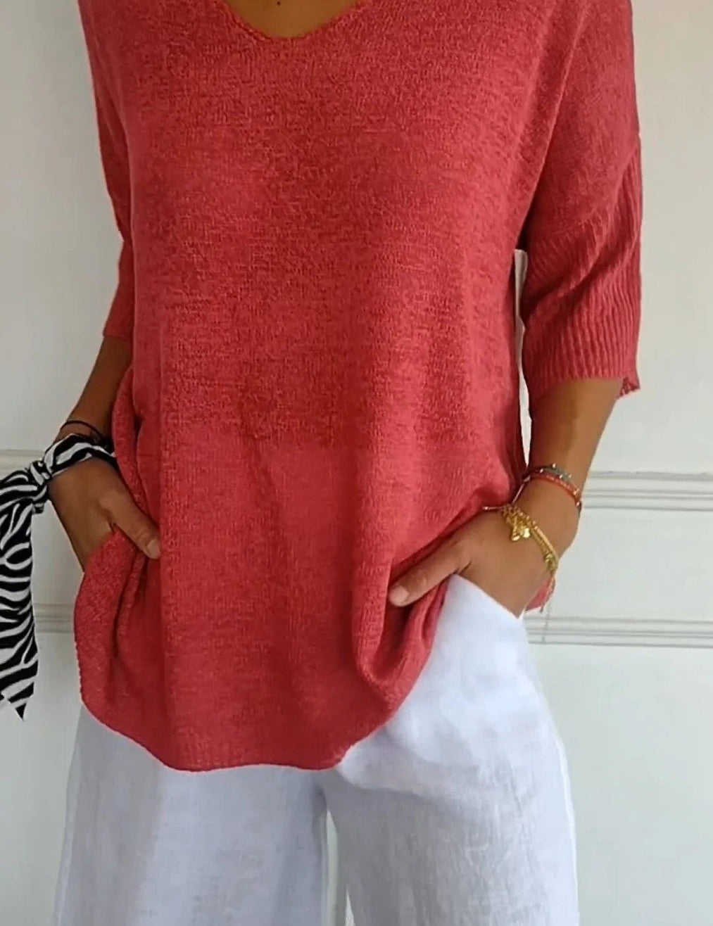 Maglia rosa a maniche corte con scollo a V, abbinata a pantaloni bianchi larghi. Look estivo casual, moda donna, abbigliamento leggero.