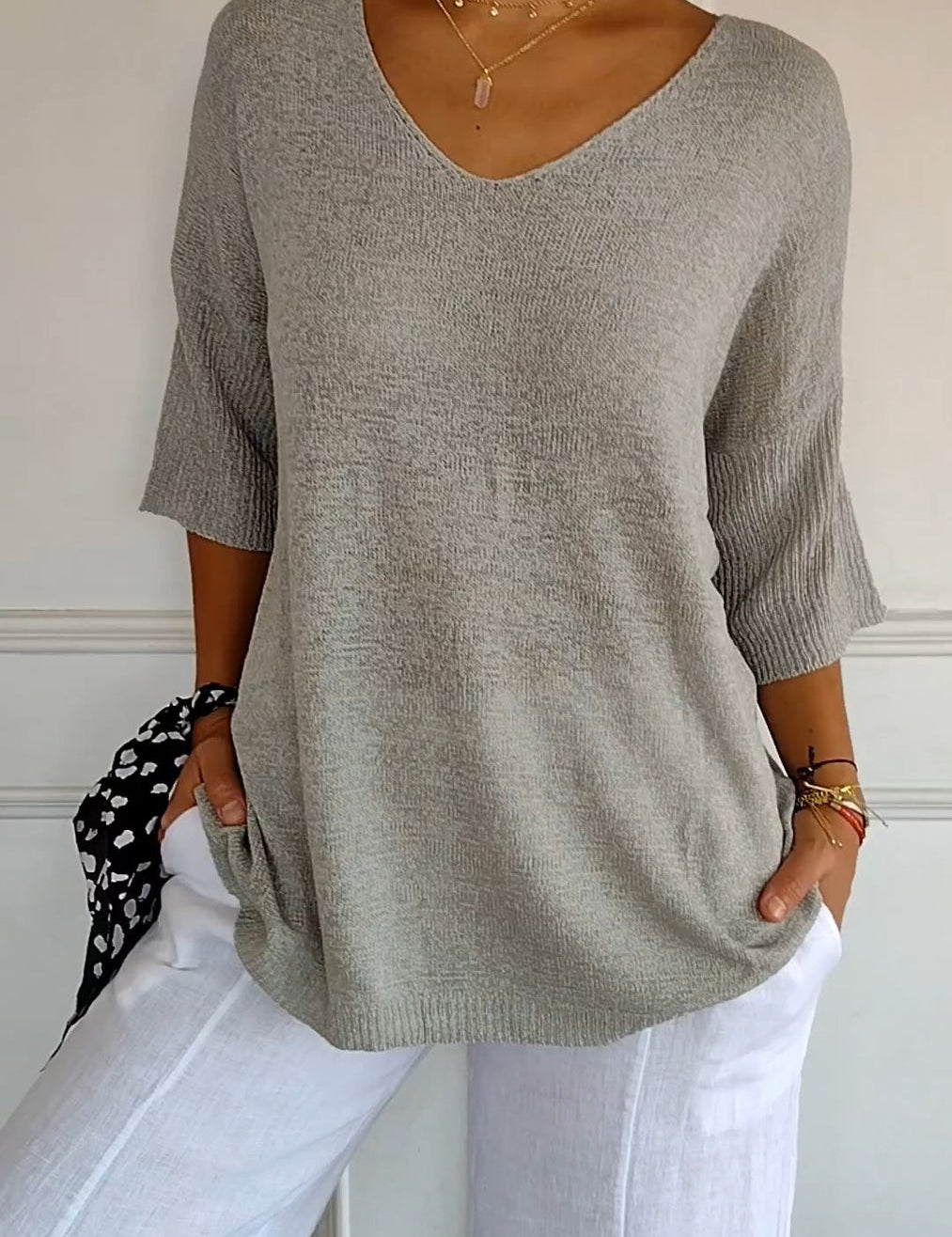 Maglione grigio donna a maniche corte, scollo a V, abbinato a pantaloni bianchi. Look casual ed elegante, moda femminile primavera estate.