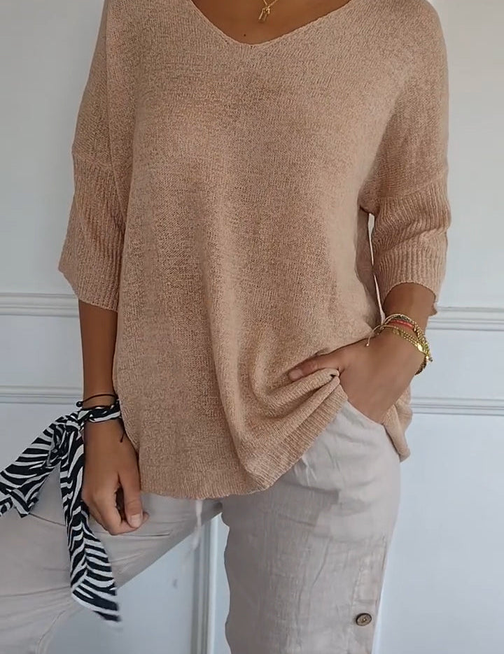 Maglia beige a maniche lunghe con scollo a V, abbinata a pantaloni chiari con bottoni laterali. Look casual ed elegante, moda donna autunno.