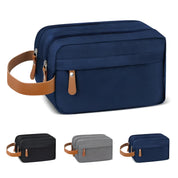 Borsa da toilette in tessuto blu con manico in pelle marrone, zip doppia, disponibile in nero, grigio e blu. Accessorio da viaggio elegante e pratico.