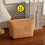 Pochette beige in tessuto trapuntato su tavolo in legno, accanto a libri e lampada. Design elegante, ideale per accessori moda.