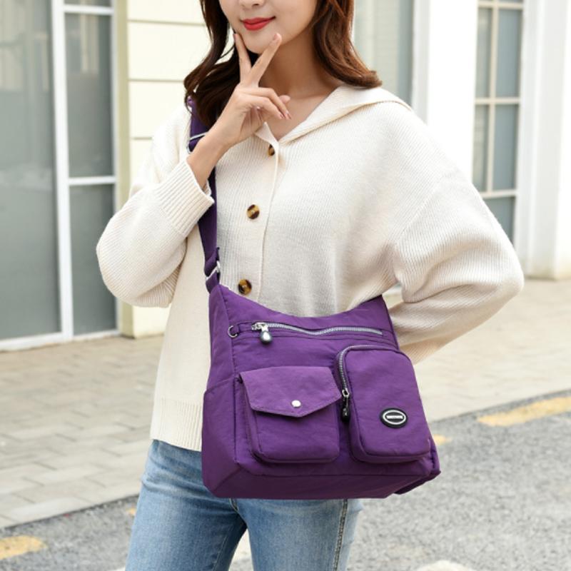 Donna con borsa a tracolla viola, tasche multiple, indossa maglione bianco e jeans. Moda casual, accessorio pratico per uso quotidiano.