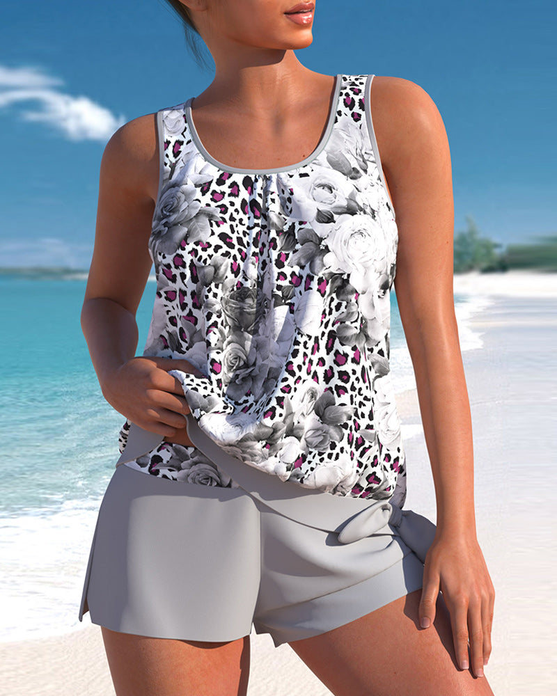Donna in spiaggia con canotta floreale bianca e nera, dettagli leopardati, e pantaloncini grigi. Moda estiva, abbigliamento casual mare.