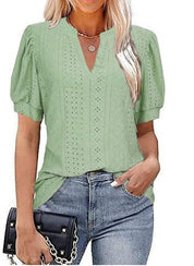Blusa verde donna con maniche a sbuffo, scollo a V, dettagli traforati, abbinata a jeans e borsa nera. Moda casual elegante.