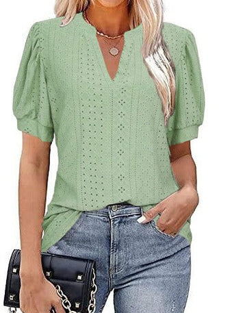 Blusa verde donna con maniche a sbuffo, scollo a V, dettagli traforati, abbinata a jeans e borsa nera. Moda casual elegante.