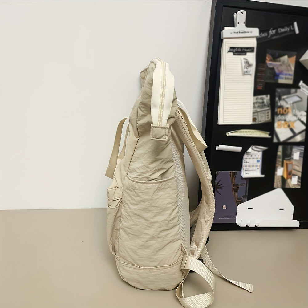 Zaino beige in tessuto morbido su tavolo, con tasche laterali e spallacci regolabili. Sfondo con bacheca nera e appunti. Accessorio moda casual.