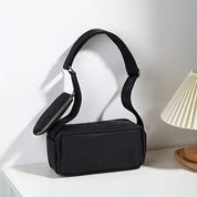 Borsa a tracolla nera elegante su tavolo bianco, design minimalista, con tasca con zip, perfetta per moda donna, accessori versatili e moderni.