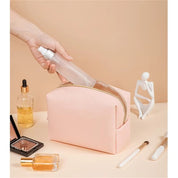 Astuccio cosmetico rosa con cerniera, contenente flacone spray trasparente. Accessori trucco e profumo su sfondo beige. Organizzatore trucco elegante.