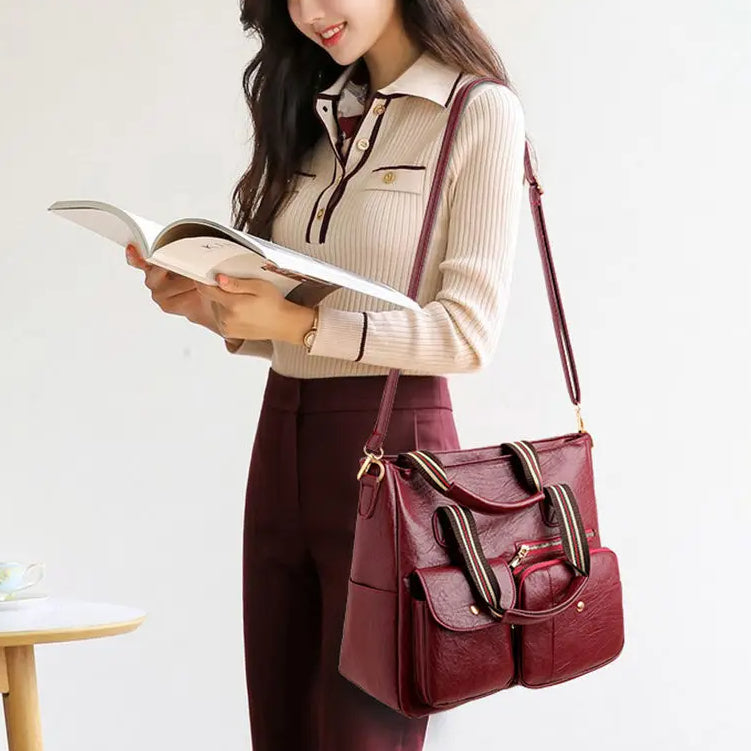 Donna con borsa a tracolla in pelle rossa, elegante e spaziosa, indossa maglione beige e pantaloni marroni, tiene un libro aperto.