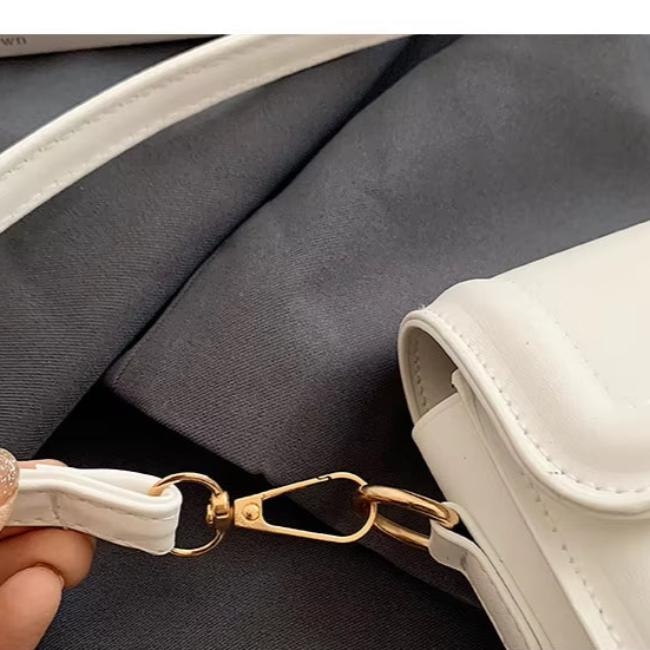 Borsa a tracolla bianca in pelle con dettagli dorati su sfondo grigio. Design elegante, accessorio moda donna, chiusura a moschettone.