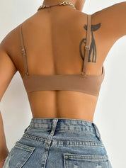 Donna di spalle con reggiseno marrone e jeans a vita alta, tatuaggio visibile sulla spalla. Moda femminile, abbigliamento casual, stile estivo.
