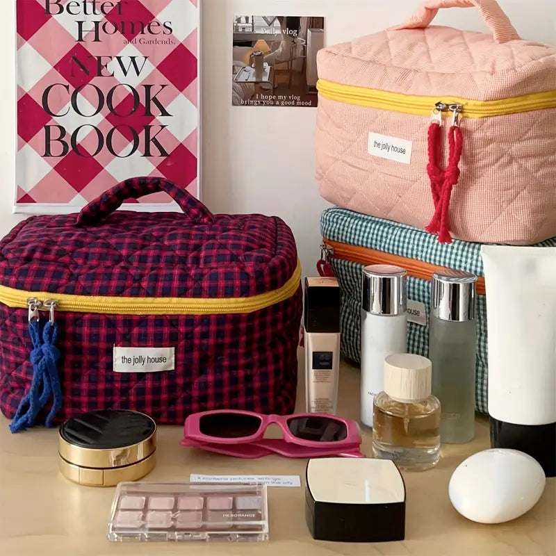 Set di borse da trucco colorate su tavolo con cosmetici, occhiali da sole e profumi. Sfondo con libro di cucina. Accessori moda e bellezza.