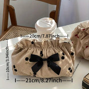 Borsa cosmetica beige a pois neri con fiocco nero, dimensioni 21x10 cm, accanto a bicchiere di caffè su tavolo in legno. Accessorio moda elegante.