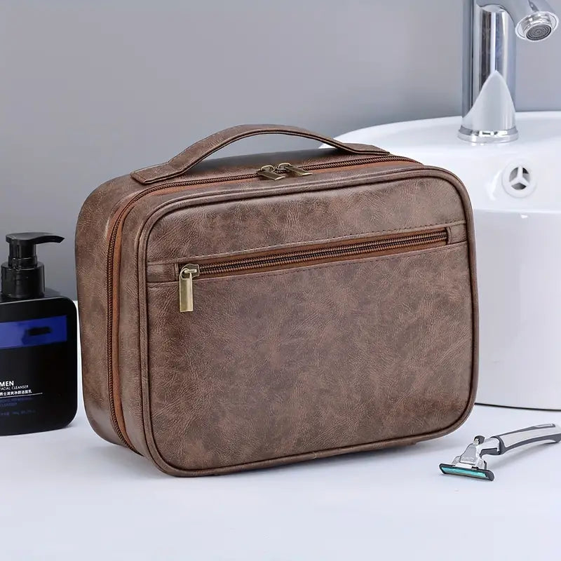 Borsa da toilette in pelle marrone con cerniera, manico superiore, accanto a lavandino e rasoio. Elegante organizer da viaggio per uomo.