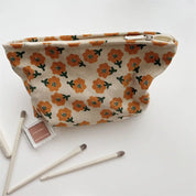 Astuccio cosmetico floreale beige con fiori arancioni, pennelli trucco e ombretto su sfondo bianco. Accessori bellezza eleganti e pratici.