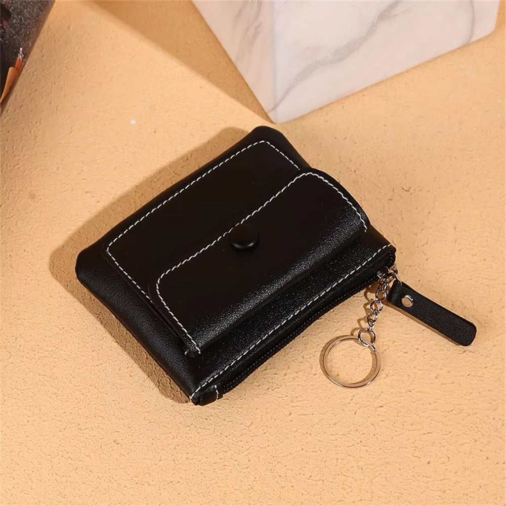 Portafoglio nero in pelle con cuciture bianche, chiusura a bottone e cerniera, anello portachiavi. Accessorio moda elegante e pratico.