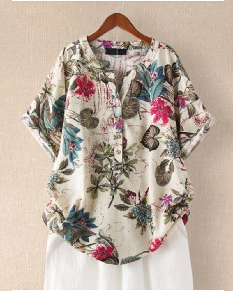 Camicia donna floreale in cotone, maniche corte, sfondo bianco, stampa colorata, casual, estiva, bottoni frontali, appesa su gruccia di legno.