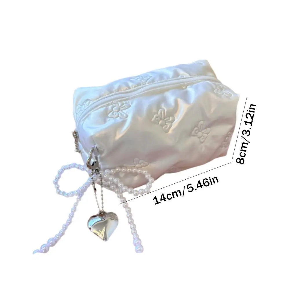 Astuccio cosmetico bianco in raso con ricami floreali, cerniera, decorazione a cuore e perline. Dimensioni: 14x8 cm. Elegante e pratico.