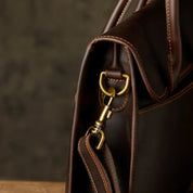 Borsa in pelle marrone scuro con dettagli in metallo dorato, design elegante e cuciture a contrasto, ideale per lavoro e viaggi.